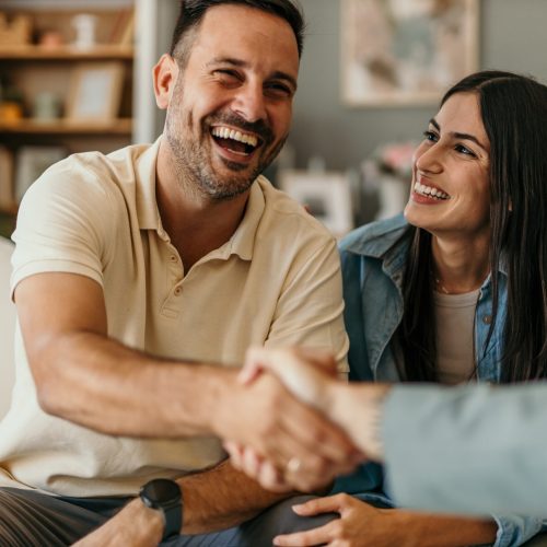 Young happy couple sitting on a sofa shaking hands with adjuster from Rocky Mountain Adjusters